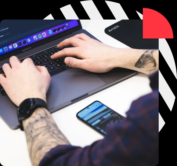 Close-up of hands typing on a laptop keyboard with a smartphone nearby