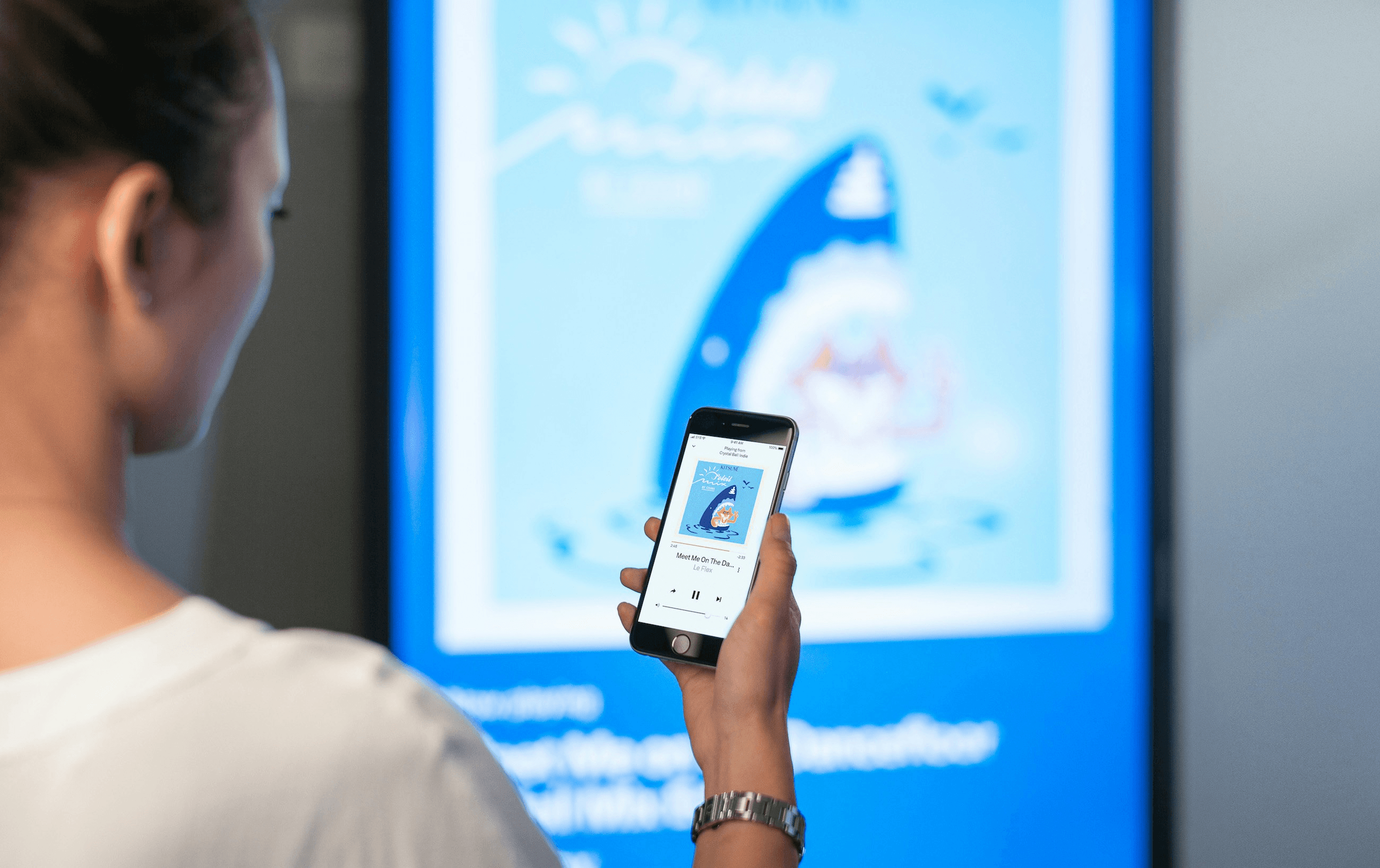 Person holding a smartphone interacting with large display showing cartoon shark graphic.