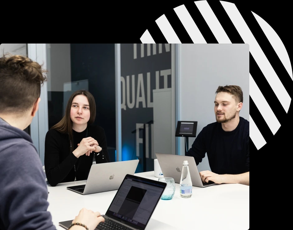 A group of three people in a meeting room, collaborating on a project with laptops in front of them.