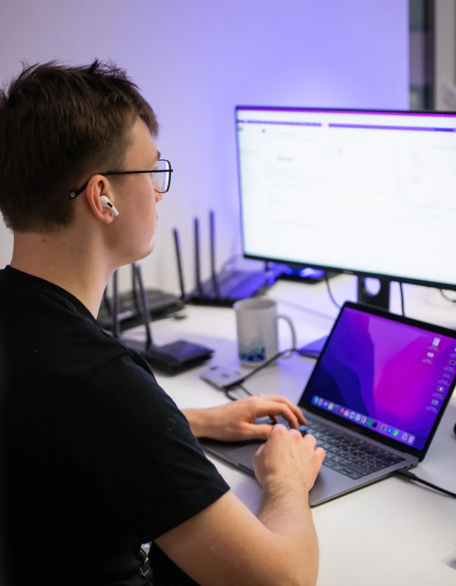 Un ingénieur réseau assis à un bureau, travaillant sur un ordinateur portable tout en regardant également un moniteur externe.