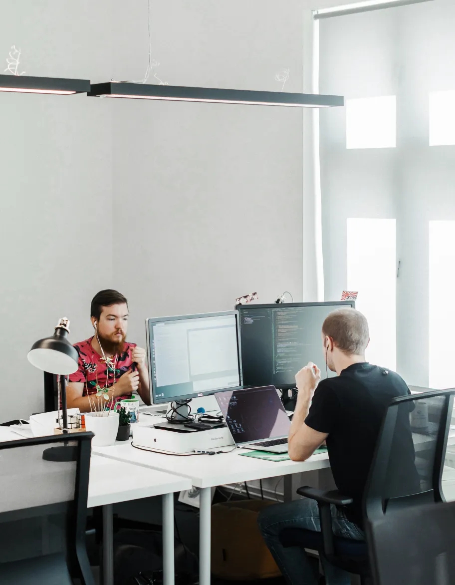 Un espacio de oficina con dos ingenieros QA sentados en sus escritorios, trabajando con computadoras.