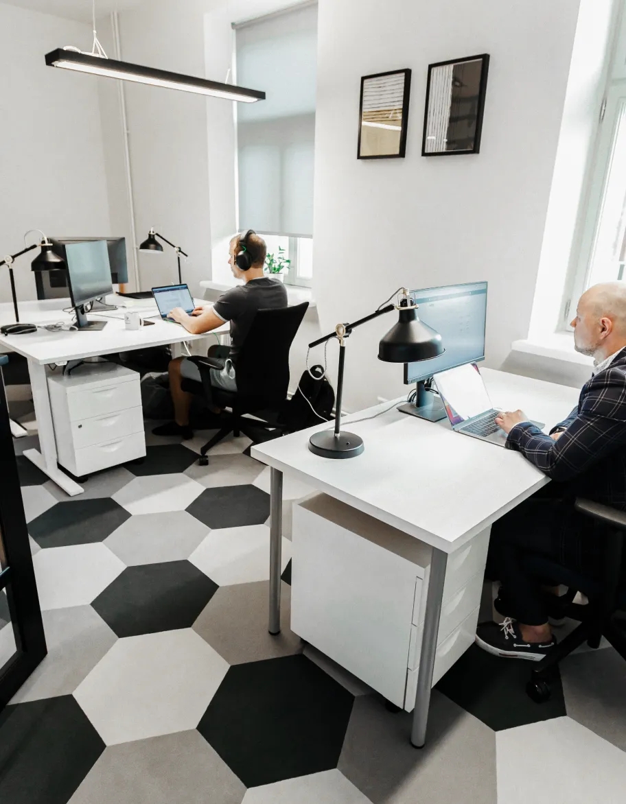 Un espacio de oficina abierto con dos ingenieros de control de calidad sentados en sus escritorios y trabajando en computadoras.