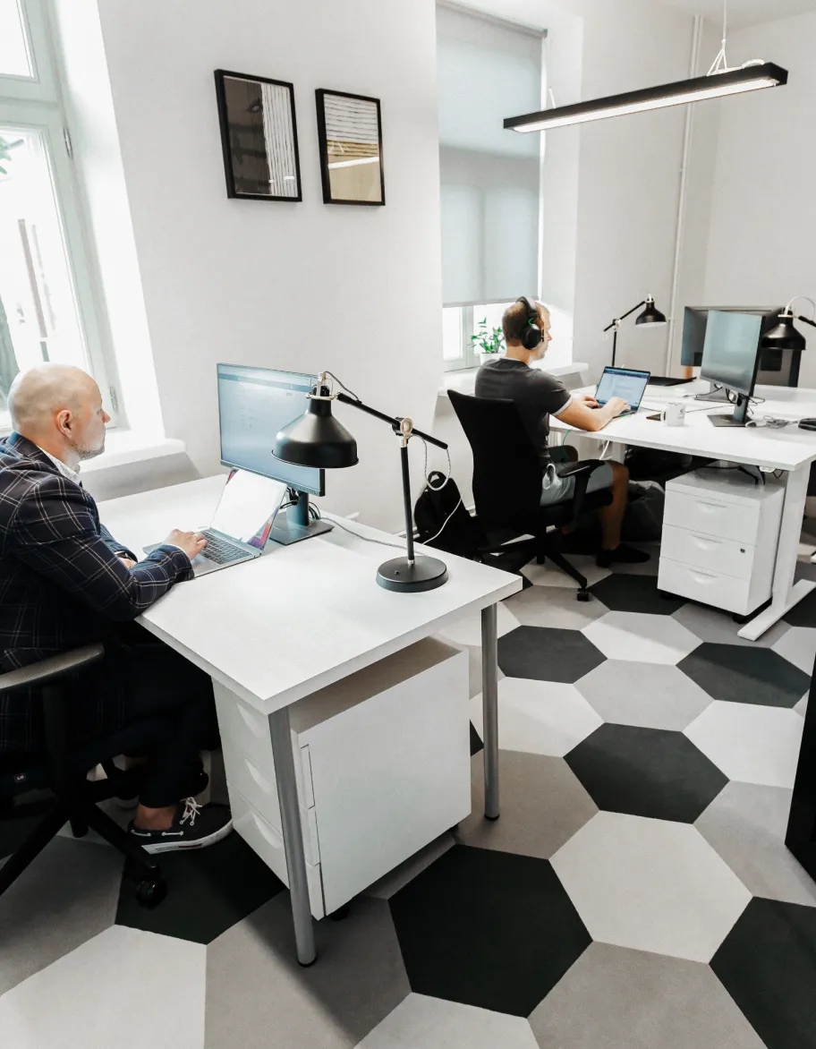 En öppen plats med två QA-ingenjörer som sitter vid skrivbord och arbetar med sina bärbara datorer.