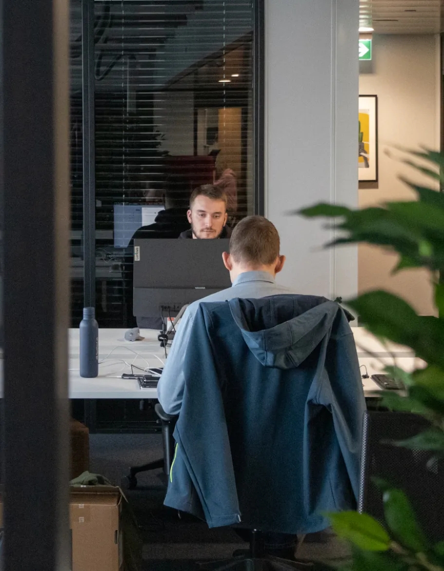 To QA-ingeniører sidder ved skriveborde på kontoret og arbejder med computere.