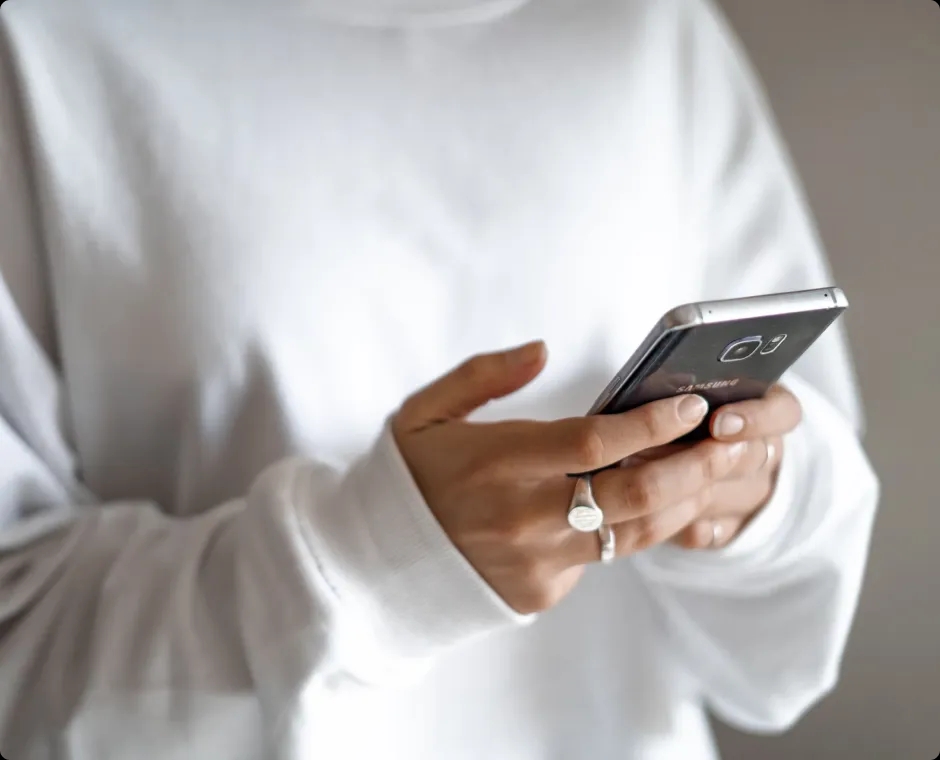 Two hands holding a phone, with a white sweatshirt visible in the background.