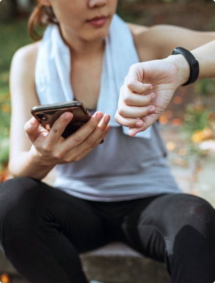 A woman holding a mobile phone and looking at her smartwatch.