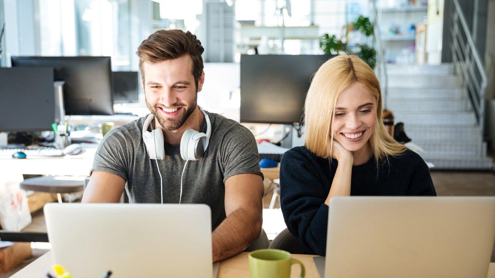 Two smiling people working together at their computers