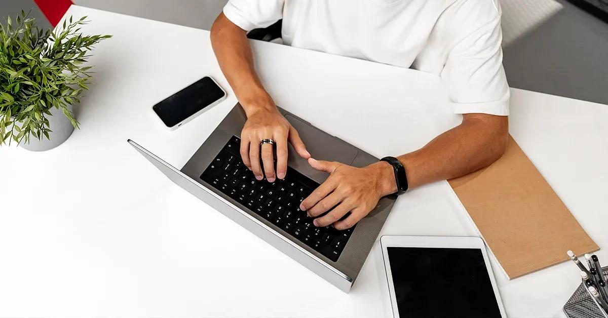 QA engineer sitting at desk working on a laptop with a smartphone and tablet next to him