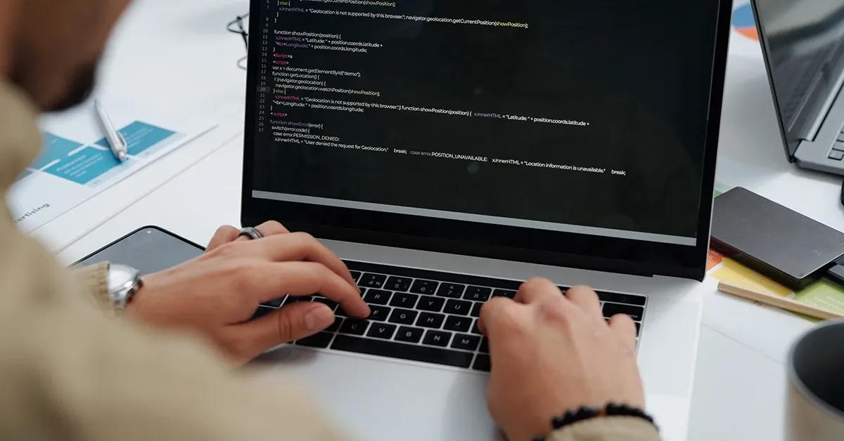 Software tester typing on laptop with code displayed on screen