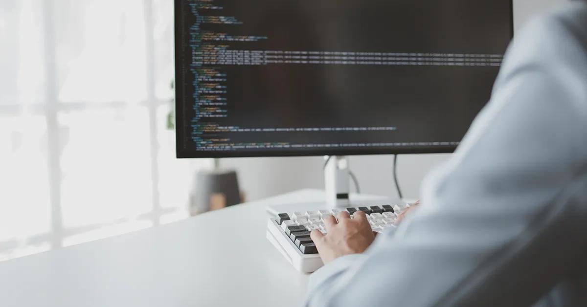 Person typing on desktop computer with code displayed on the screen