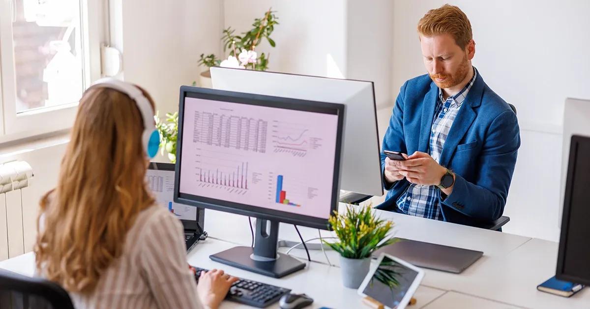 Two people working in an office and using various devices