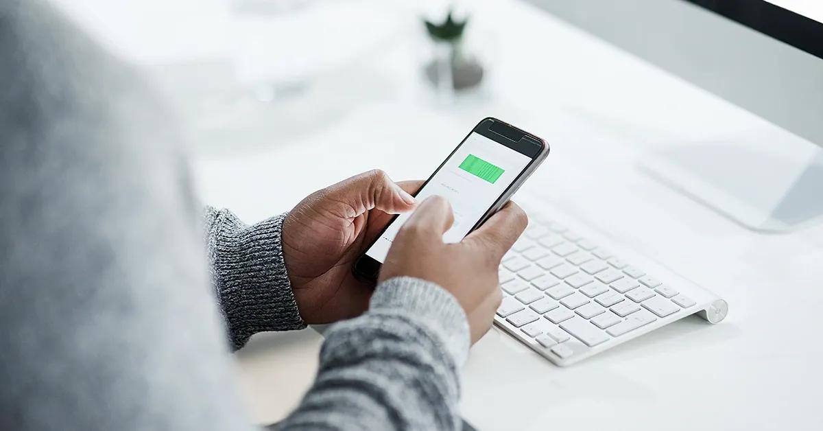 Closeup of person tapping on mobile phone while seated at desk