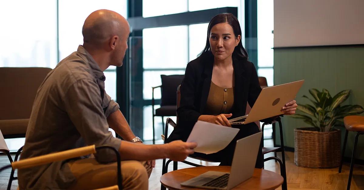 A man and woman with laptops talking to each other