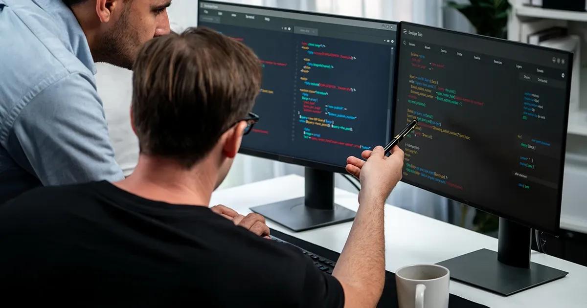 Two men looking at computer screens and reviewing code scripts.