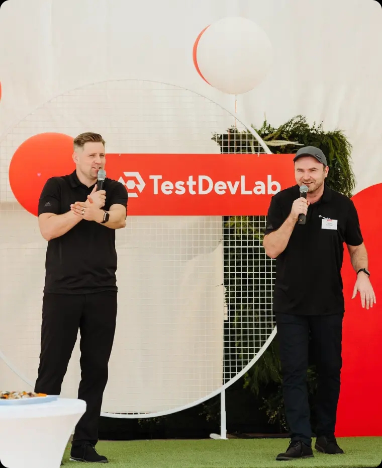 TestDevLab co-CEOs speaking at a company event with a TestDevLab banner behind them.