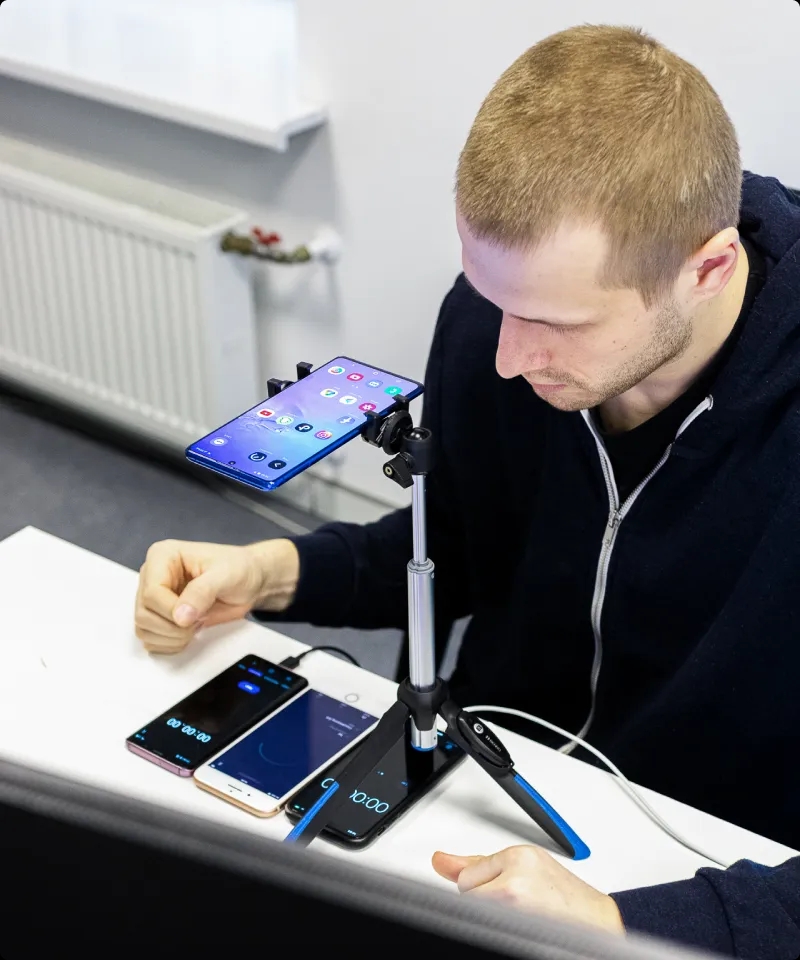 A QA engineer working with 4 mobile phones on the desk, with one placed in a tripod.
