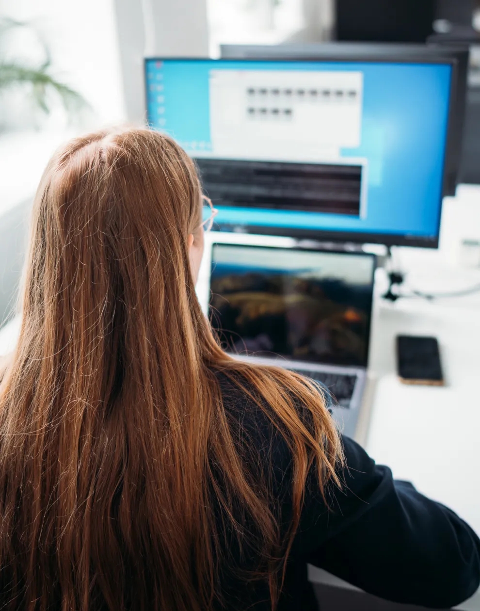 Une femme assise à un bureau, travaillant sur un ordinateur portable connecté à un grand écran.