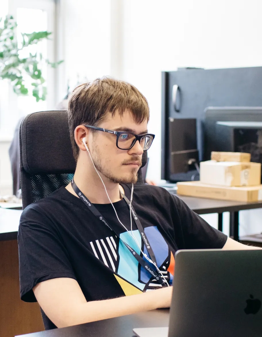 Un ingénieur QA portant des écouteurs et des lunettes, assis à un bureau et travaillant sur un ordinateur portable dans un environnement de bureau.