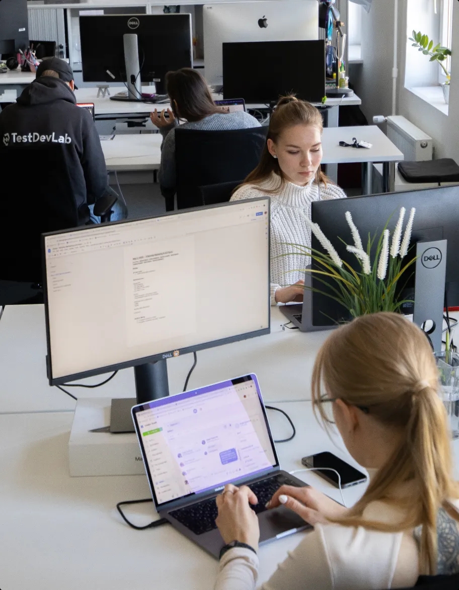 An open office space with multiple people sitting at their desks and working on laptops.