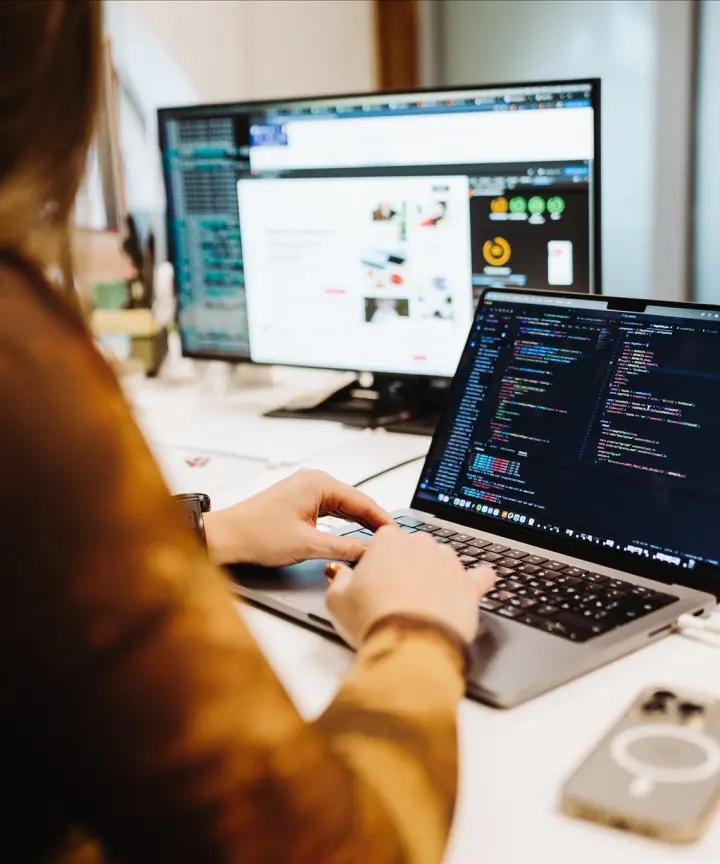 Person working at a desk with a laptop and desktop computer.