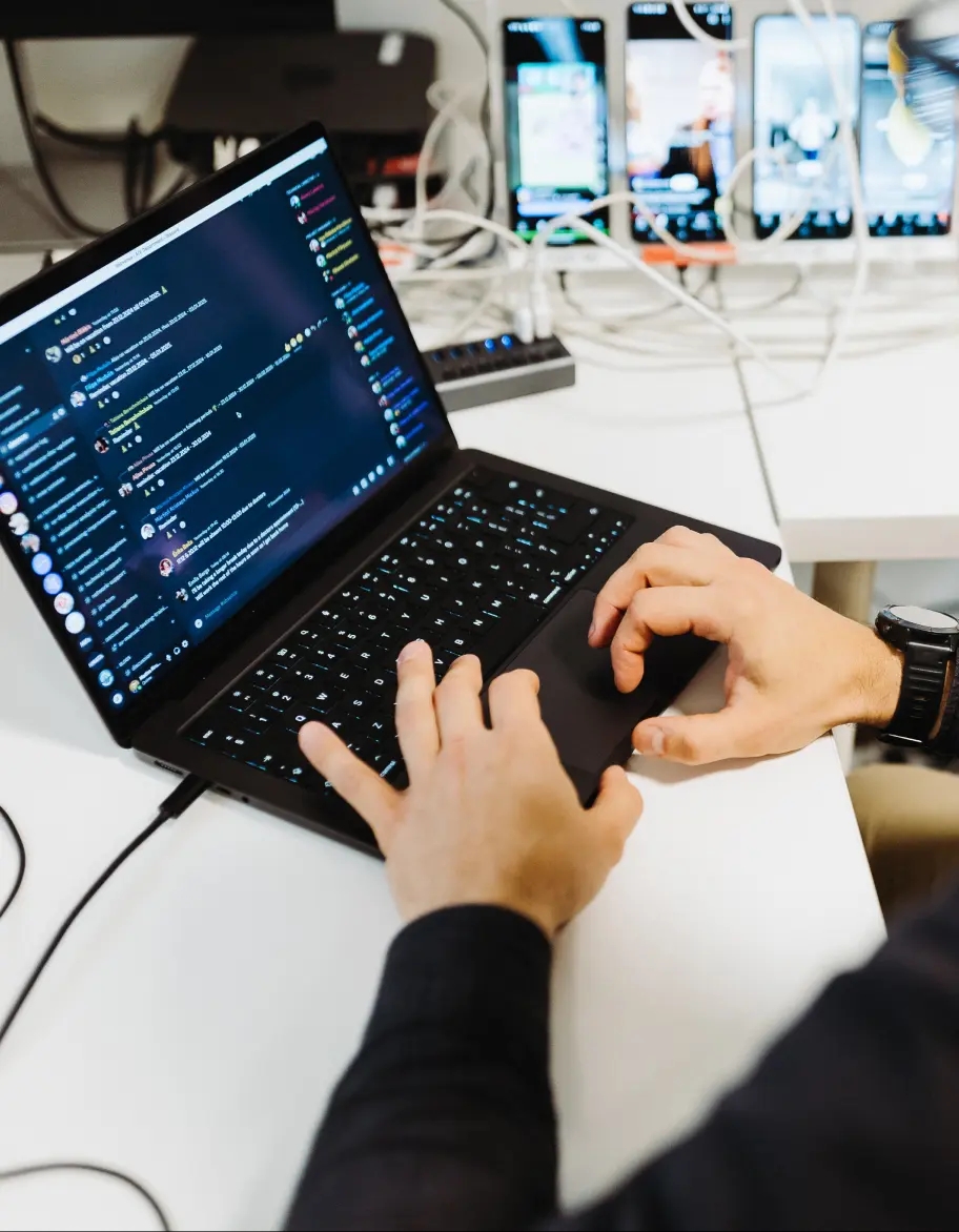 Person working on a laptop at a desk with mobile phones on stands.