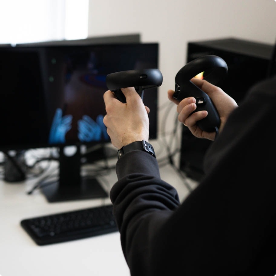 QA engineer facing a computer screen and holding VR controllers in both hands.