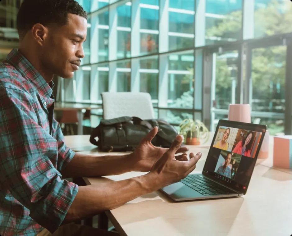 A man sitting by a window, engaged in a video conference on his laptop.