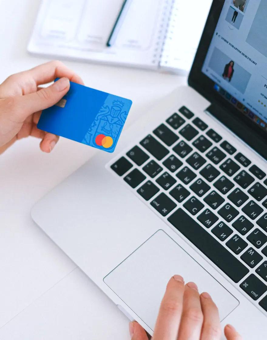 A person holding a blue bank card while shopping on a laptop