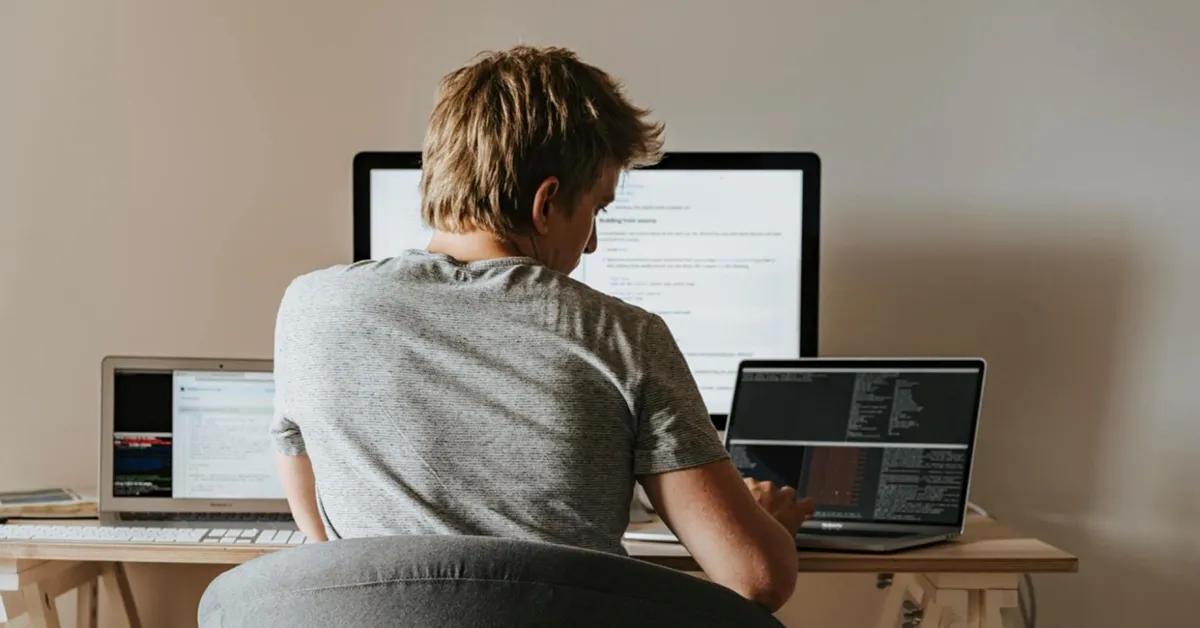 Software tester performing software testing on two laptops and one desktop