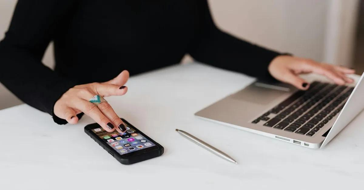A woman working at her office desk, using a laptop and a phone