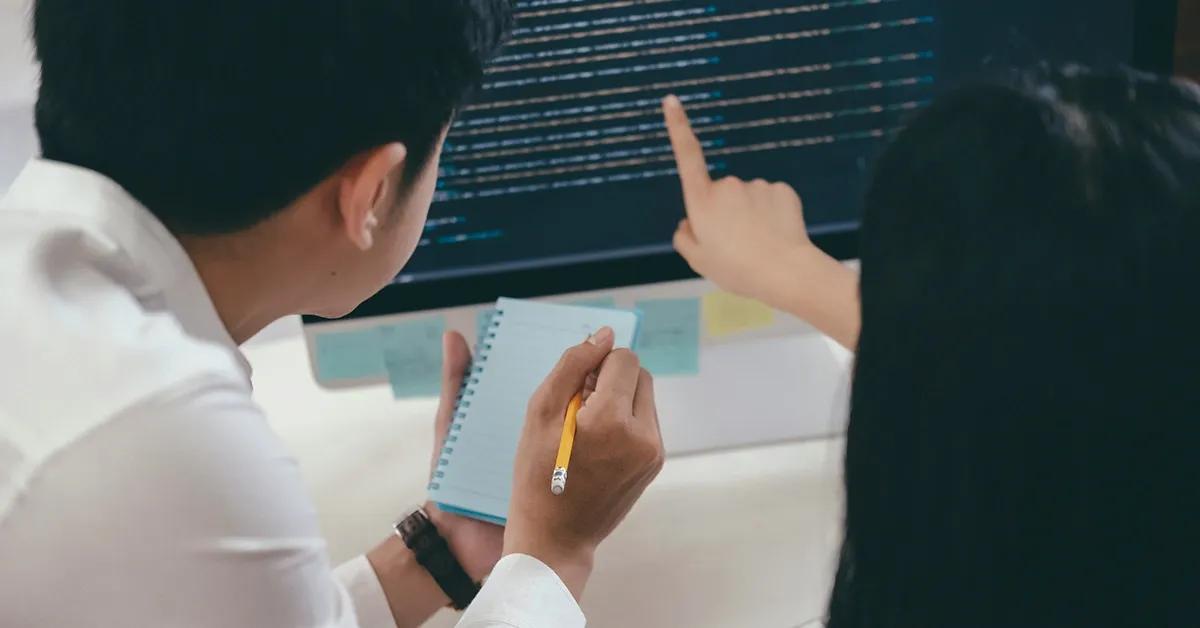 Two young professionals looking at code lines