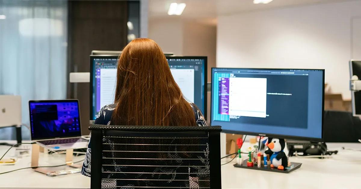Woman sitting at her work desk with multiple screens, engaged in tasks