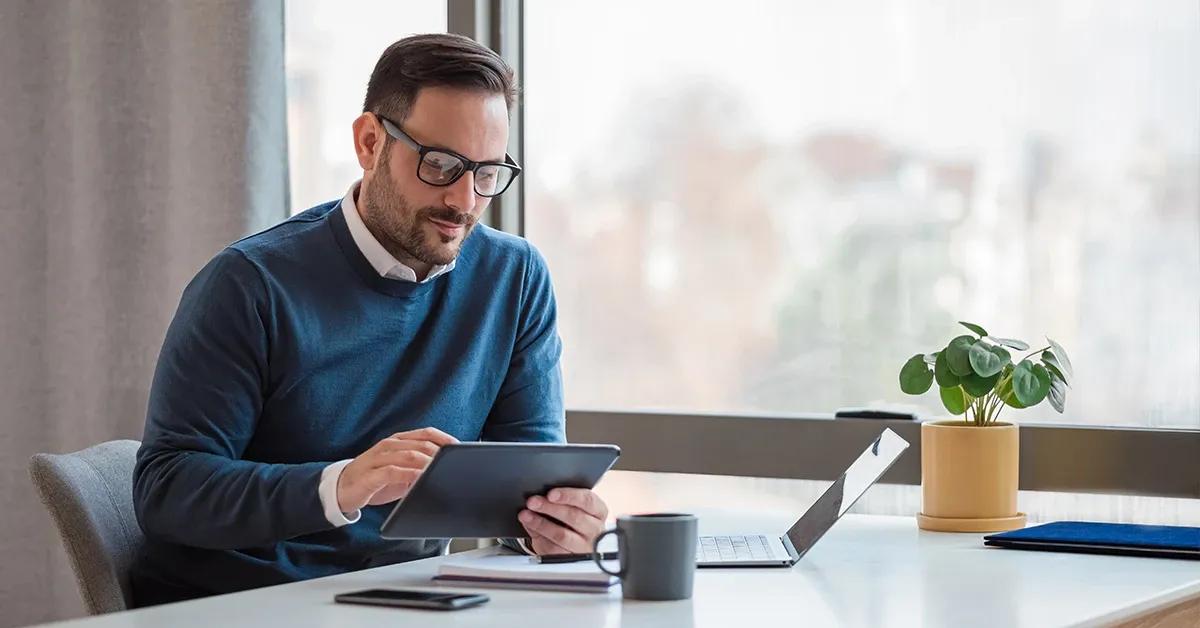A man sitting at a desk, using a tablet and a laptop