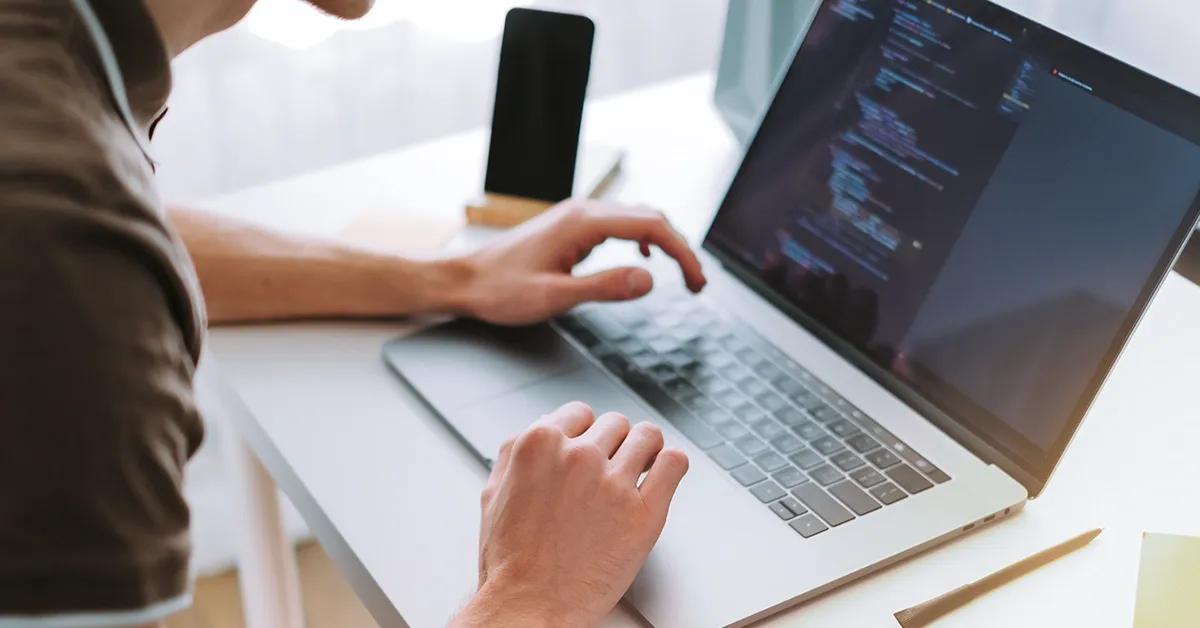 Person sitting at desk working on a laptop with code shown on screen