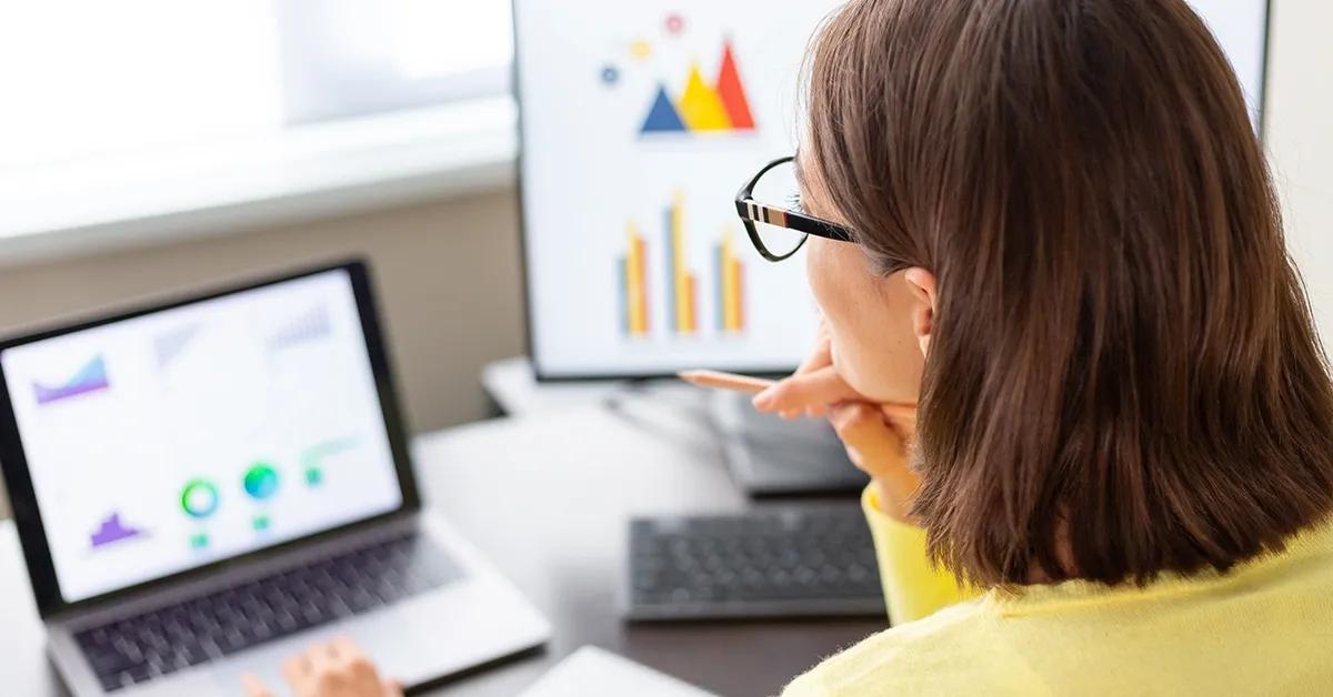Woman looking at laptop screen with a desktop computer next to it