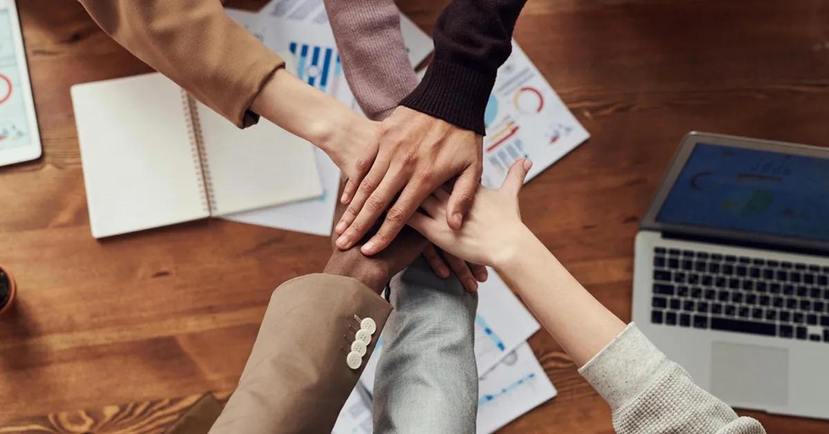 Top view of a group of people placing their hands together in a stack over a desk