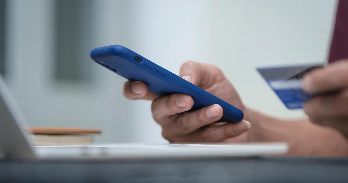 A woman using a credit card and a phone for online purchases