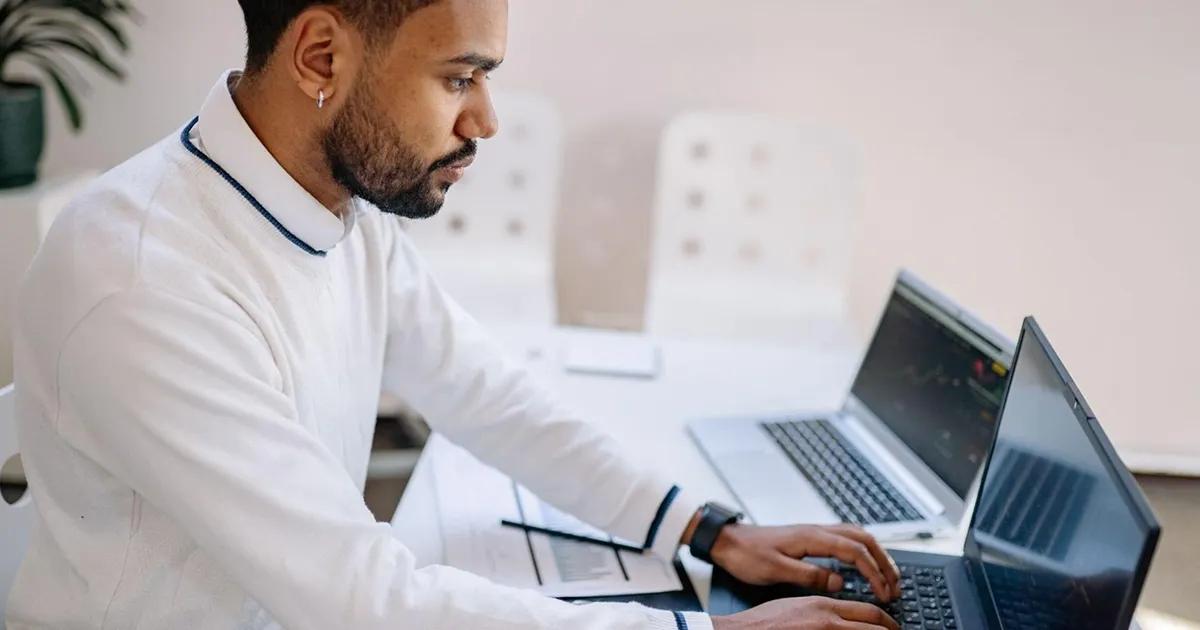 Man sitting at desk with two laptops and typing on one of them