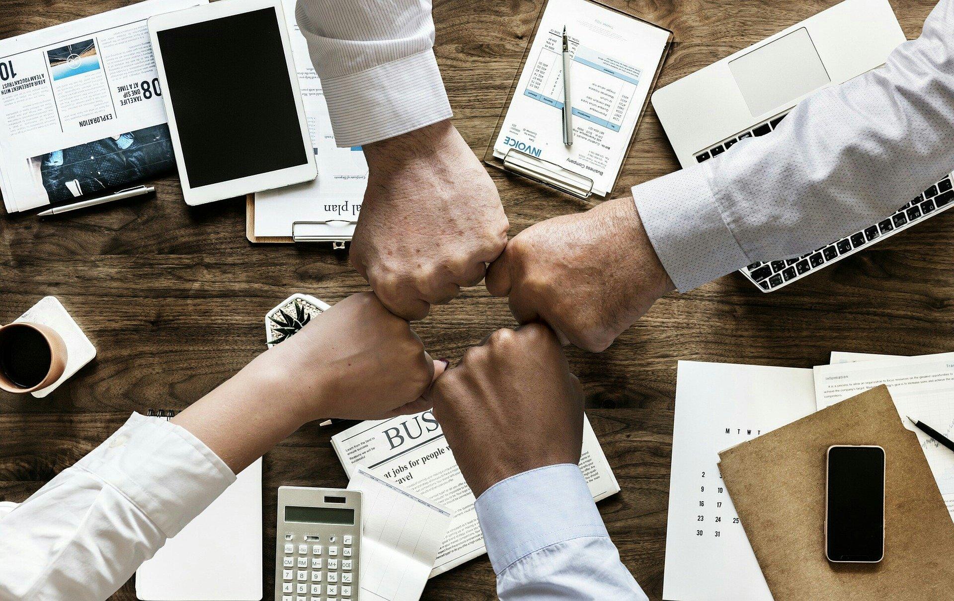 Four people with their arms over a desk greeting each other